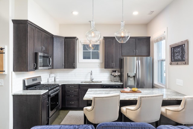 kitchen with decorative light fixtures, sink, backsplash, stainless steel appliances, and light stone countertops