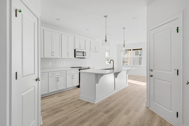 kitchen featuring a kitchen bar, sink, decorative light fixtures, a center island with sink, and white cabinets