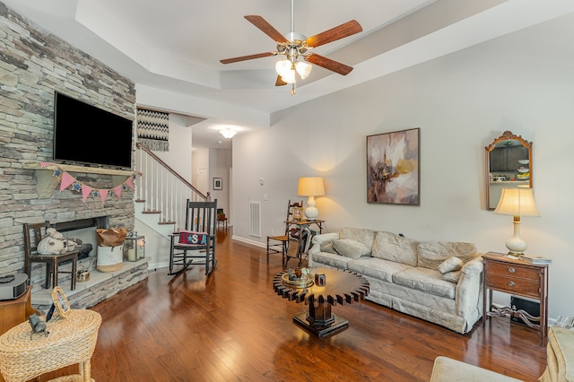 living room featuring a fireplace, ceiling fan, a raised ceiling, and dark wood-type flooring