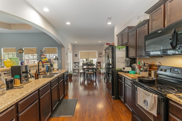 kitchen with dark wood-type flooring, light stone countertops, black appliances, dark brown cabinetry, and sink