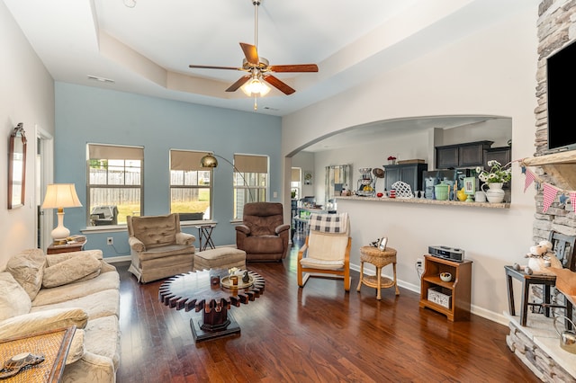 living room with dark wood-type flooring, ceiling fan, and a raised ceiling