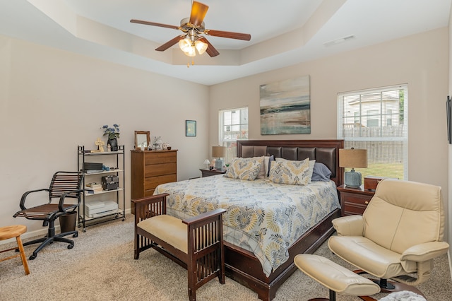 carpeted bedroom with ceiling fan and a raised ceiling