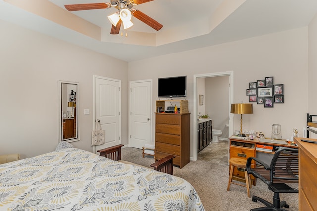 carpeted bedroom with a raised ceiling, ensuite bathroom, and ceiling fan