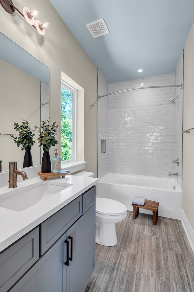 full bathroom with vanity, tiled shower / bath, hardwood / wood-style flooring, and toilet