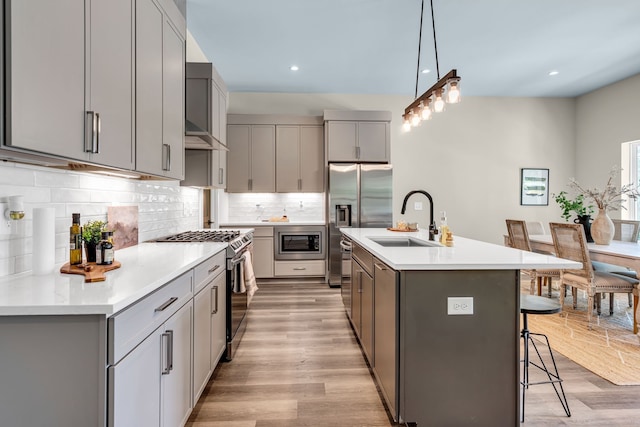 kitchen with a breakfast bar, light hardwood / wood-style flooring, stainless steel appliances, decorative backsplash, and sink