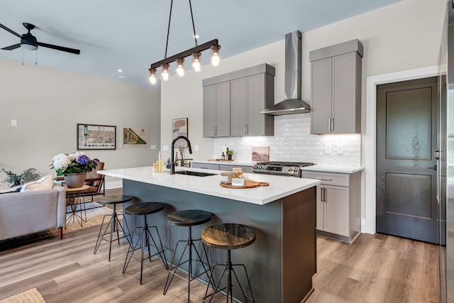 kitchen with pendant lighting, light hardwood / wood-style floors, gray cabinets, stainless steel gas range oven, and wall chimney exhaust hood