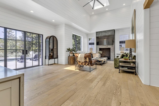 living room with a towering ceiling, plenty of natural light, a large fireplace, and light wood-type flooring