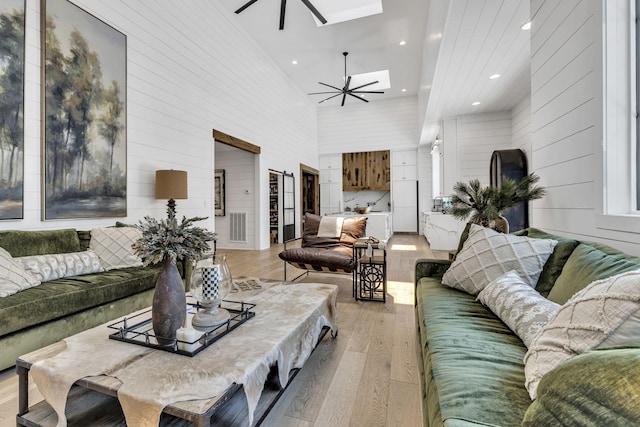 living room featuring a high ceiling, a skylight, ceiling fan, and light wood-type flooring