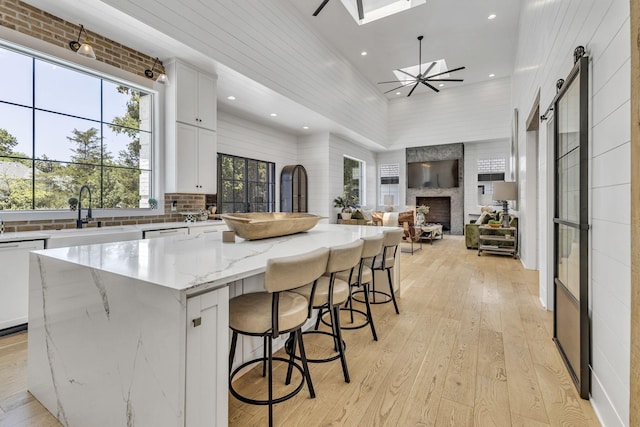 kitchen with sink, dishwasher, a large island, light stone countertops, and white cabinets