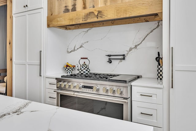 kitchen with white cabinetry, double oven range, light stone countertops, and decorative backsplash