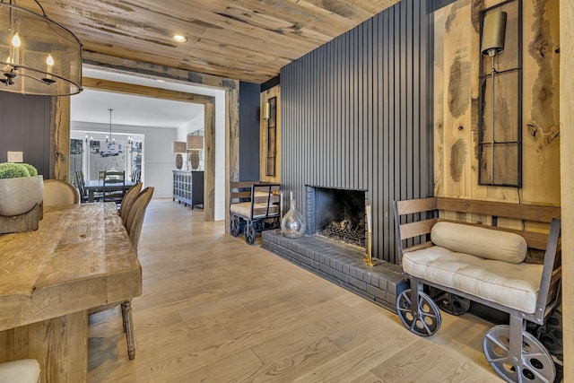 living room featuring a brick fireplace, wooden ceiling, a chandelier, and light hardwood / wood-style floors