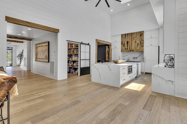 kitchen with ceiling fan, light stone countertops, white cabinets, a barn door, and light wood-type flooring