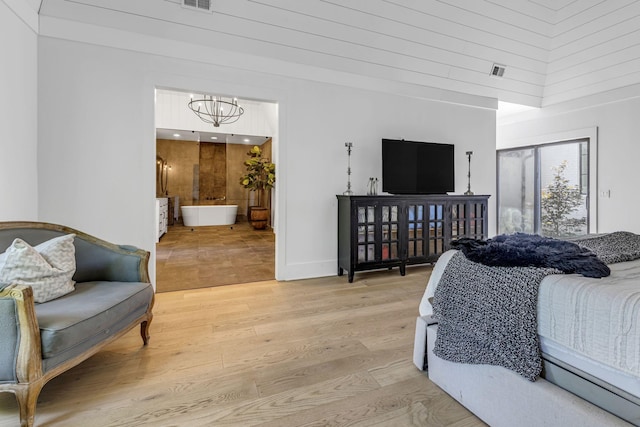 bedroom with ensuite bathroom, a towering ceiling, a notable chandelier, and light hardwood / wood-style floors