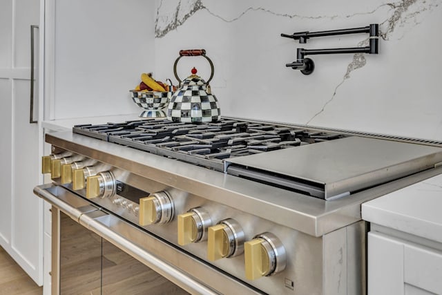 details featuring white cabinetry, light stone counters, high end stove, and light hardwood / wood-style flooring