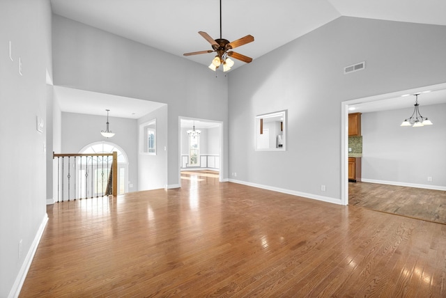 unfurnished living room featuring a high ceiling, ceiling fan with notable chandelier, and hardwood / wood-style flooring