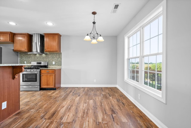 kitchen with an inviting chandelier, gas stove, tasteful backsplash, decorative light fixtures, and wall chimney range hood