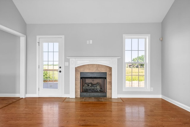 unfurnished living room featuring hardwood / wood-style flooring, vaulted ceiling, a tiled fireplace, and a healthy amount of sunlight