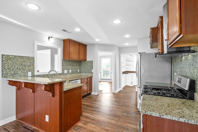 kitchen featuring kitchen peninsula, white dishwasher, dark wood-type flooring, light stone countertops, and a kitchen breakfast bar