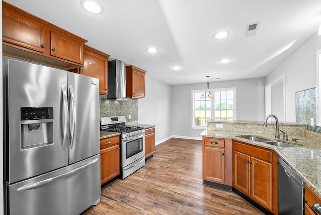 kitchen with pendant lighting, wall chimney exhaust hood, wood-type flooring, stainless steel appliances, and sink