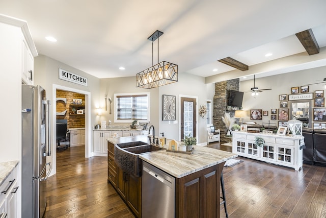 kitchen with ceiling fan with notable chandelier, an island with sink, beam ceiling, dark hardwood / wood-style floors, and appliances with stainless steel finishes