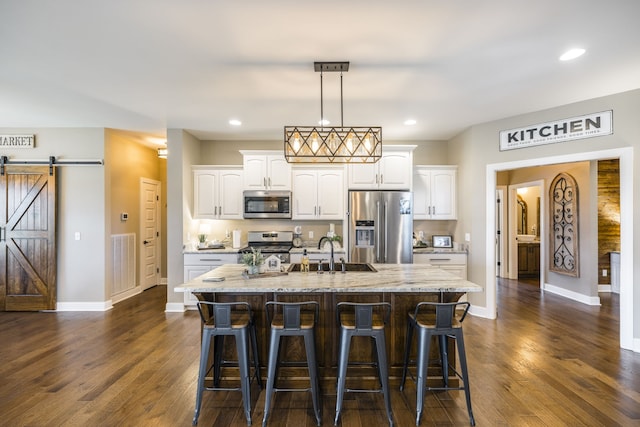 kitchen with white cabinetry, stainless steel appliances, an island with sink, a barn door, and dark wood-type flooring