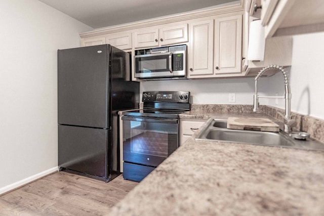 kitchen with black appliances, light hardwood / wood-style floors, cream cabinetry, and sink