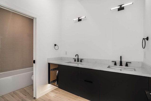 bathroom with a sink, toilet, wood finished floors, and double vanity