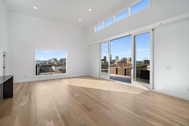 unfurnished living room with baseboards, a view of city, a towering ceiling, and light wood finished floors