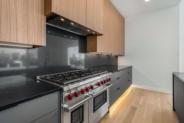 kitchen with range with two ovens, light wood-style floors, modern cabinets, and custom range hood