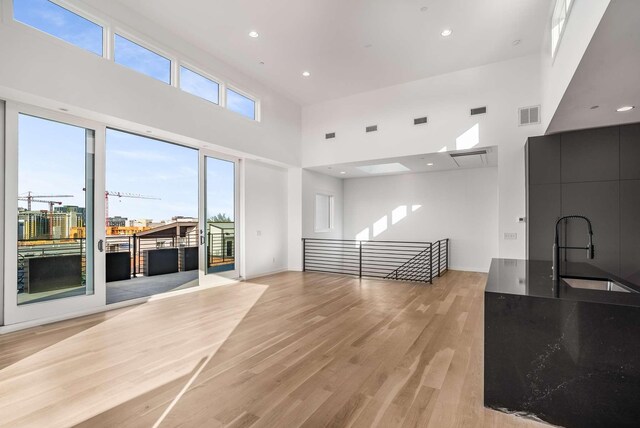 living room with recessed lighting, visible vents, light wood-style floors, and a towering ceiling