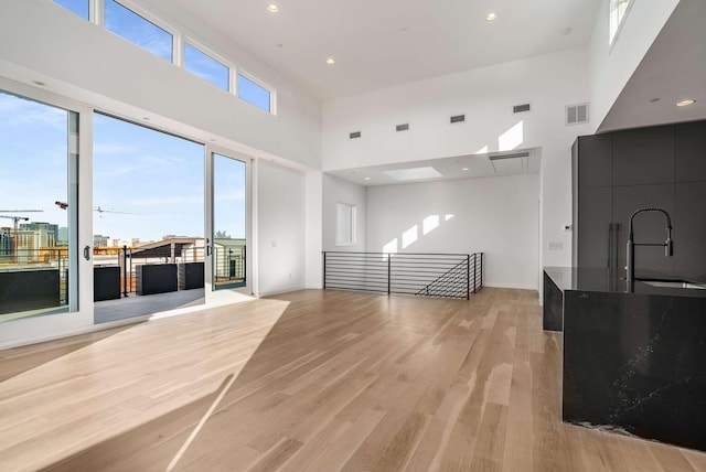 unfurnished living room featuring visible vents, light wood-type flooring, recessed lighting, a towering ceiling, and a sink