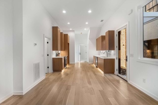 kitchen with visible vents, brown cabinets, a sink, light wood-style floors, and light countertops