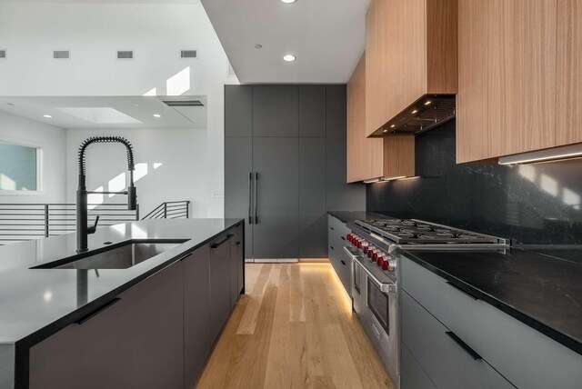 kitchen with range with two ovens, modern cabinets, wall chimney exhaust hood, and a sink