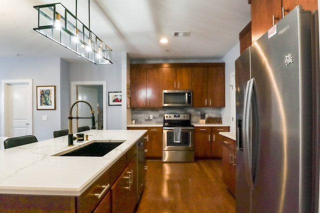 kitchen with an island with sink, sink, appliances with stainless steel finishes, backsplash, and dark wood-type flooring