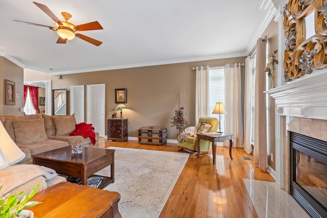 living room featuring crown molding, a high end fireplace, light hardwood / wood-style floors, and ceiling fan