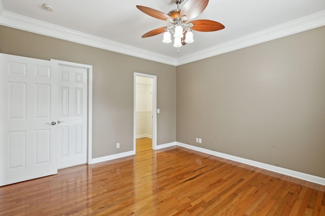 unfurnished bedroom with a walk in closet, wood-type flooring, ornamental molding, a closet, and ceiling fan