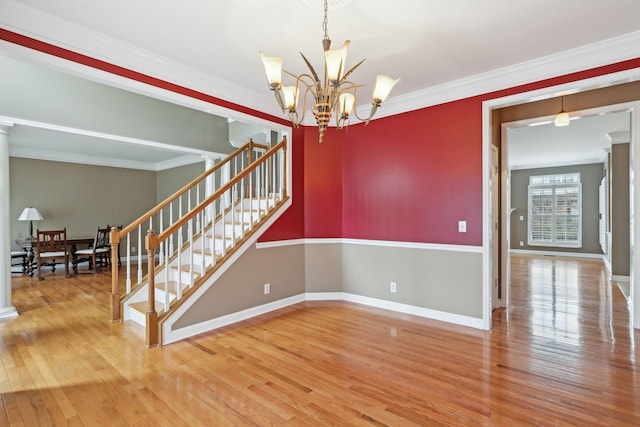 spare room with hardwood / wood-style flooring, crown molding, decorative columns, and a notable chandelier