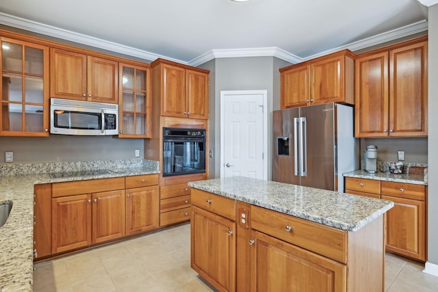 kitchen featuring light stone countertops, ornamental molding, black appliances, and a center island