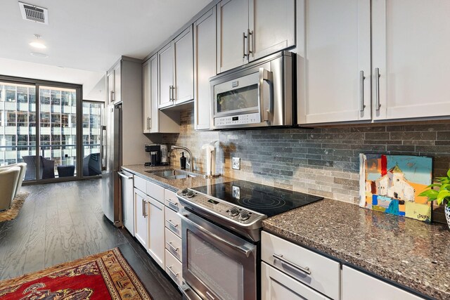 kitchen featuring tasteful backsplash, stainless steel appliances, sink, dark stone countertops, and dark wood-type flooring