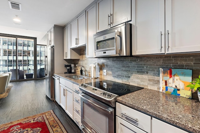 kitchen with dark hardwood / wood-style floors, sink, dark stone countertops, backsplash, and stainless steel appliances