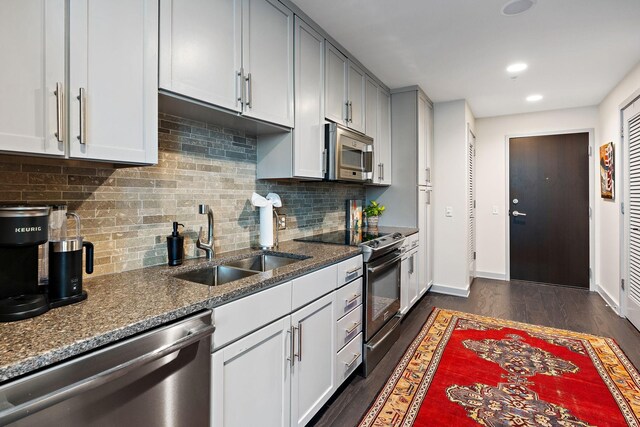 kitchen with dark wood-type flooring, backsplash, appliances with stainless steel finishes, stone countertops, and sink