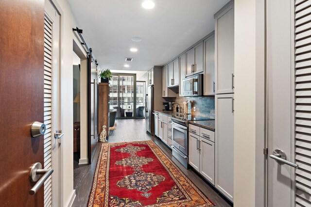 kitchen featuring tasteful backsplash, a barn door, dark hardwood / wood-style floors, stainless steel appliances, and gray cabinetry