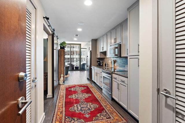 kitchen with dark wood-type flooring, appliances with stainless steel finishes, a barn door, and tasteful backsplash