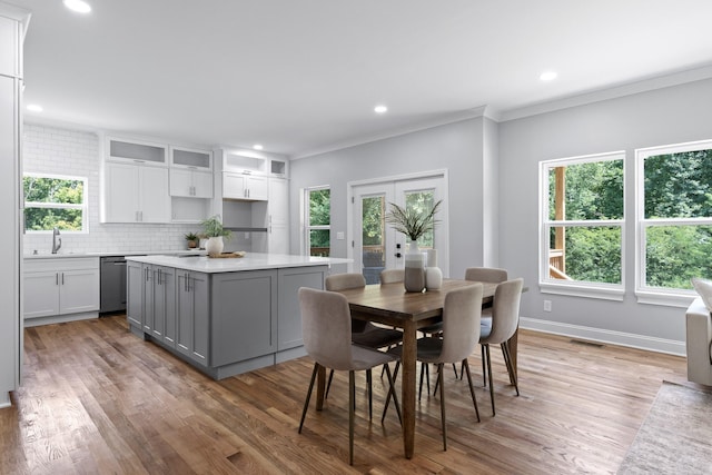 kitchen featuring stainless steel dishwasher, backsplash, gray cabinetry, ornamental molding, and hardwood / wood-style flooring