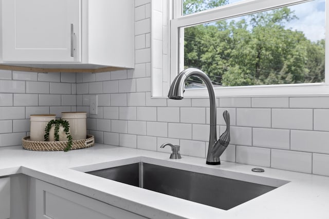 interior details featuring backsplash, white cabinets, and sink