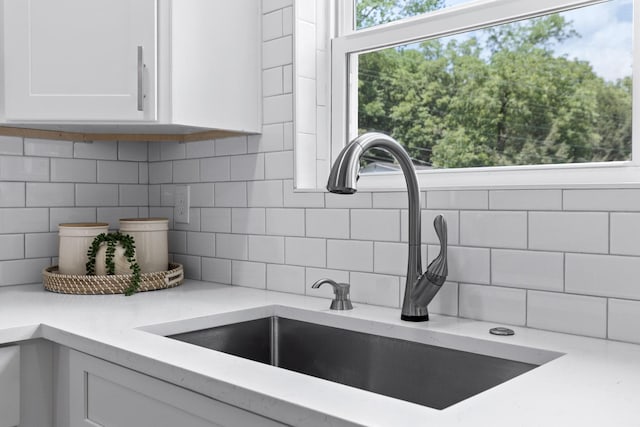 room details with sink, white cabinetry, light stone countertops, and backsplash