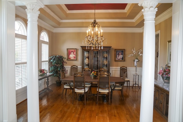 dining area featuring wood-type flooring, a raised ceiling, ornate columns, and ornamental molding