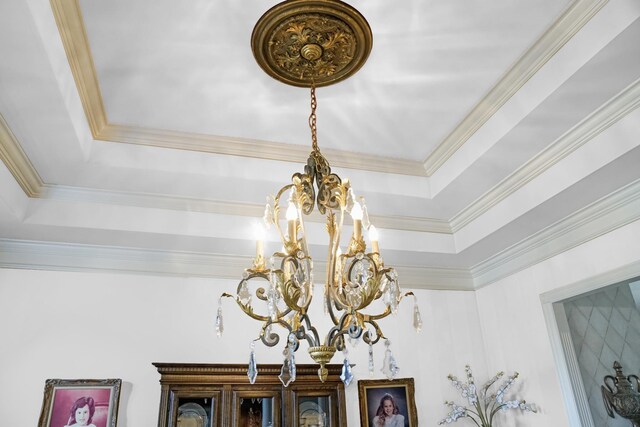 interior details with an inviting chandelier, a raised ceiling, and ornamental molding