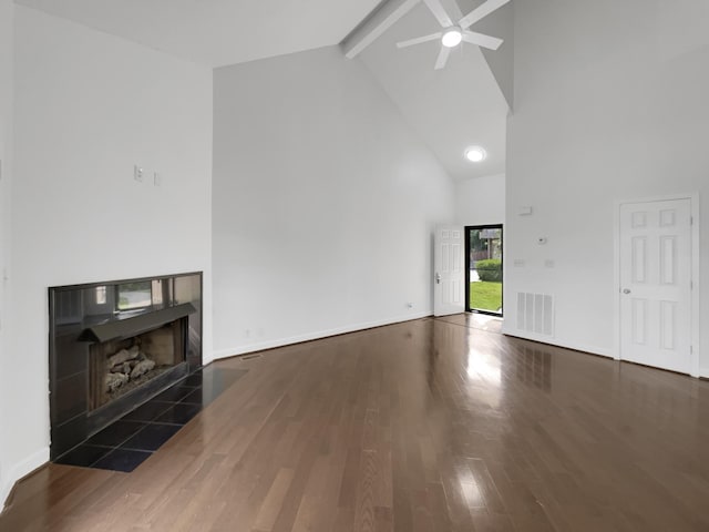 unfurnished living room featuring dark hardwood / wood-style flooring, beamed ceiling, ceiling fan, high vaulted ceiling, and a tiled fireplace