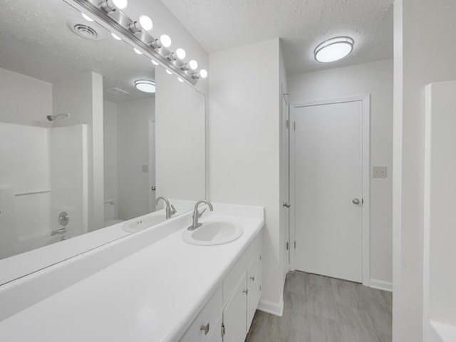 bathroom with a textured ceiling, shower / bath combination, and vanity